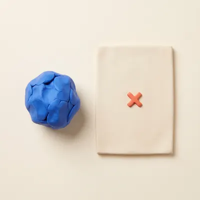 Clay crumpled paper ball beside a flat sheet with a cross mark